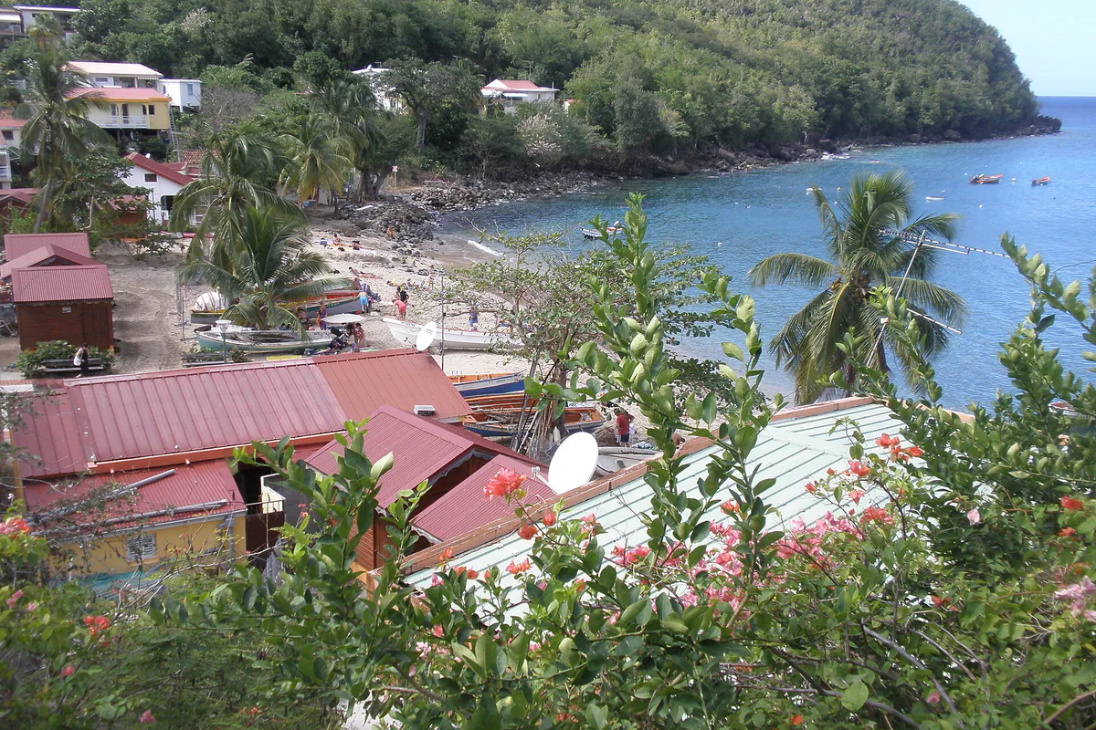 Petite plage de sable clair, barques et maisons au bord de l’eau à Anse Dufour
